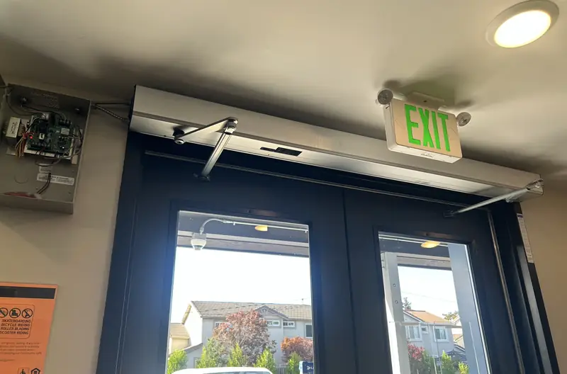 Automatic door hardware and exit sign above a commercial entrance